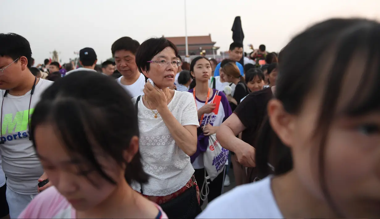 Warga berjalan menghadiri upacara pengibaran bendera saat fajar setelah kematian mantan perdana menteri China Li Peng di Lapangan Tiananmen Beijing (24/7/2019). Li Peng meninggal dunia akibat menderita kanker kandung kemih. (AFP Photo/Greg Baker)