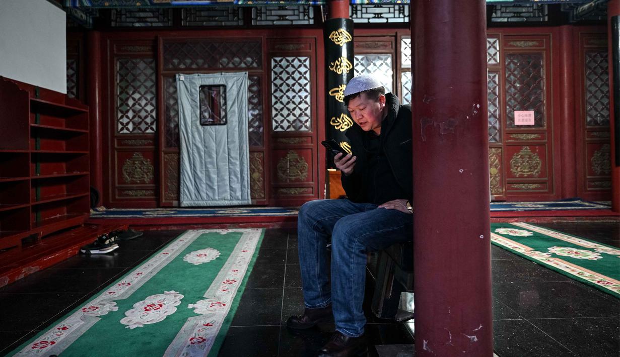 Mereka dikenal sangat ramah, berfokus pada perdagangan dan kuliner halal, serta hidup damai dengan mengadopsi gaya lokal dalam arsitektur masjid yang unik. Tampak dalam foto, seorang pria Muslim etnis Hui Tiongkok membaca Al-Quran di ponselnya di sebuah masjid selama minggu terakhir bulan suci Ramadhan di Beijing pada 17 Maret 2026. (Adek BERRY/AFP)