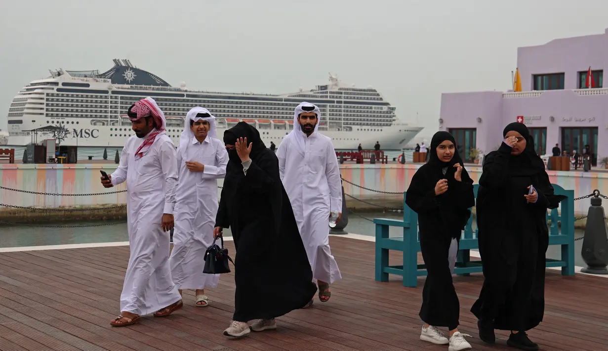 <p>Pria dan wanita berjalan selama ajang Piala Dunia 2022 Qatar di Distrik Mina Doha pada 10 Desember 2022. Letaknya yang sempurna di dekat perairan Doha di mana Anda dapat melihat pemandangan yang ditempatkan kapal pesiar seperti MSC World Europa, berfungsi sebagai pilihan akomodasi bagi penggemar sepak bola. (AFP/Christina Assi)</p>