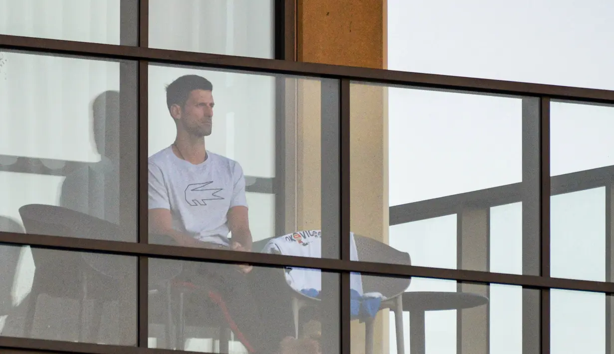 Petenis pria peringkat satu dunia, Novak Djokovic duduk di balkon salah satu hotel tempat karantina, Adelaide, Australia, Senin (18/1/2021). (Foto: AFP/Brenton Edwards)