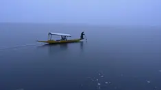 Seorang pria mengendarai perahu di dekat bagian beku danau Dal setelah hujan salju lebat di Srinagar (16/1/2020). Banyak daerah terpencil di lembah telah terputus akibat hujan salju lebat tersebut. (AFP Photo/Tauseef Mustafa)