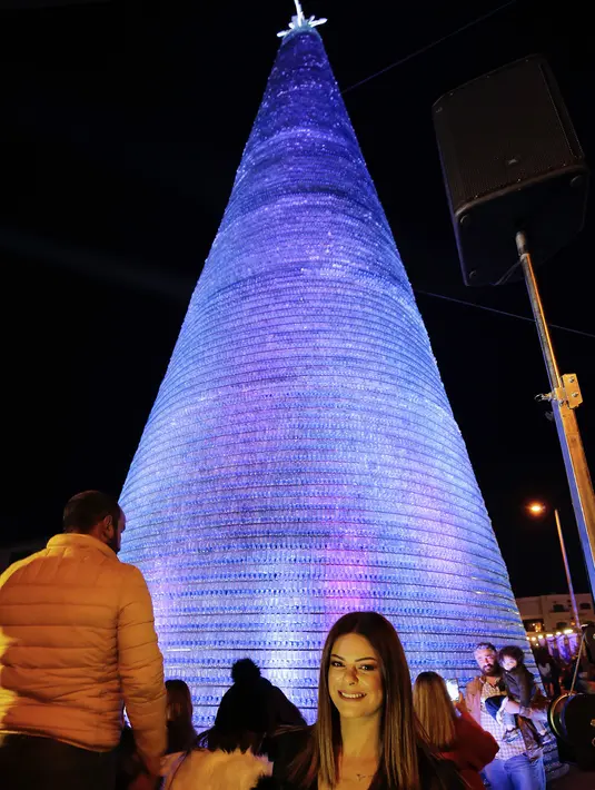 Caroline Chaptini berpose di depan Pohon Natal raksasa yang terbuat dari botol plastik di kota Chekka, Lebanon, 15 Desember 2019. Tujuan proyek ini adalah untuk memecahkan Guinness World Record sebelumnya, yakni pohon Natal yang dibangun dari 98.000 botol di Meksiko. (Ibrahim CHALHOUB/AFP)