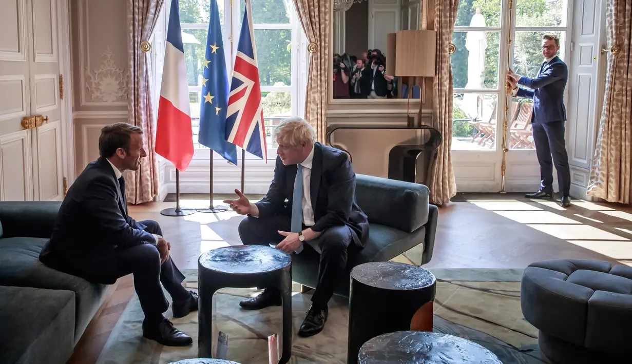 Presiden Prancis Emmanuel Macron berbincang dengan PM Inggris, Boris Johnson dalam kunjungan kenegaraan di Istana Elysee, Paris, Kamis (22/8/2019). Dalam pertemuan, Johnson tertangkap kamera bercanda ke arah kamera dan meletakkan kakinya di meja kopi. (Christophe Petit Tesson, Pool via AP)