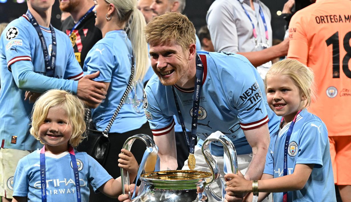Pemain Manchester City, Kevin De Bruyne bersama kedua anaknya berpose dengan trofi Liga Champions setelah mengalahkan Inter Milan di Ataturk Olympic Stadium, Istanbul, Turki, 10 Juni 2023. De Bruyne diketahui merupakan kapten dengan gaji tertinggi di Liga Inggris. Ia mendapatkan bayaran sebesar 400 ribu pounds per pekan di Etihad Stadium. Sementara itu, pemain Belgia tersebut masih memiliki kontrak hingga 2025 mendatan. (AFP/Paul Ellis)