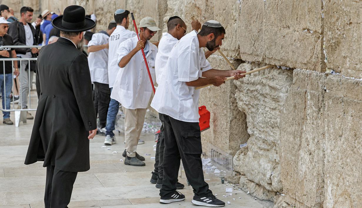 Pekerja pemeliharaan di Tembok Barat, situs paling suci di mana orang Yahudi diizinkan untuk berdoa, melakukan pembersihan untuk menghilangkan dari celah-celah pesan agama dan doa yang tertulis di selembar kertas yang ditinggalkan oleh ribuan jemaah sebelumnya, di kota tua Yerusalem pada 20 September 2022. (AFP/Ahmad Gharabli)