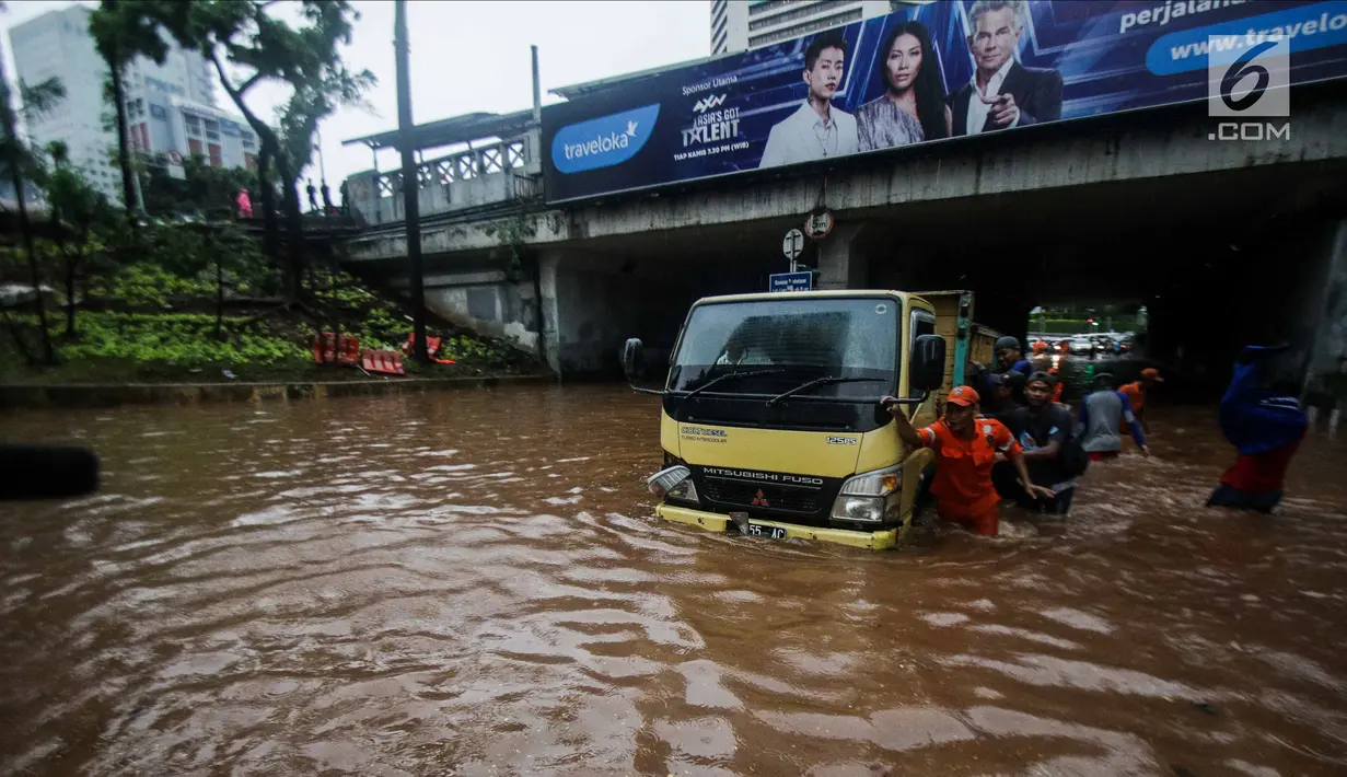 Petugas dibantu warga mendorong truk yang mogok akibat terjebak banjir di terowongan Dukuh Atas, Jakarta, Senin (11/12). Hujan lebat yang mengguyur ibu kota mengakibatkan genangan hingga satu meter di lokasi tersebut. (Liputan6.com/Faizal Fanani)