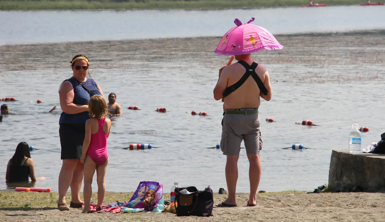 Seorang pria menggunakan payung melindungi kepala dan anak yang dipegangnya dari matahari di Goose Lake di Anchorage, Alaska (5/7/2019). Cuaca panas diperkirakan akan berlanjut hingga minggu depan. (AP Photo/Mark Thiessen)