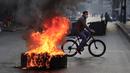 Seorang pria mengendarai sepeda melewati ban yang dibakar oleh pengunjuk rasa di sepanjang jalan utama selama protes terhadap kenaikan harga konsumen dan jatuhnya mata uang lokal di Beirut, Lebanon, Senin (29/11/2021). (AP Photo/Hussein Malla)