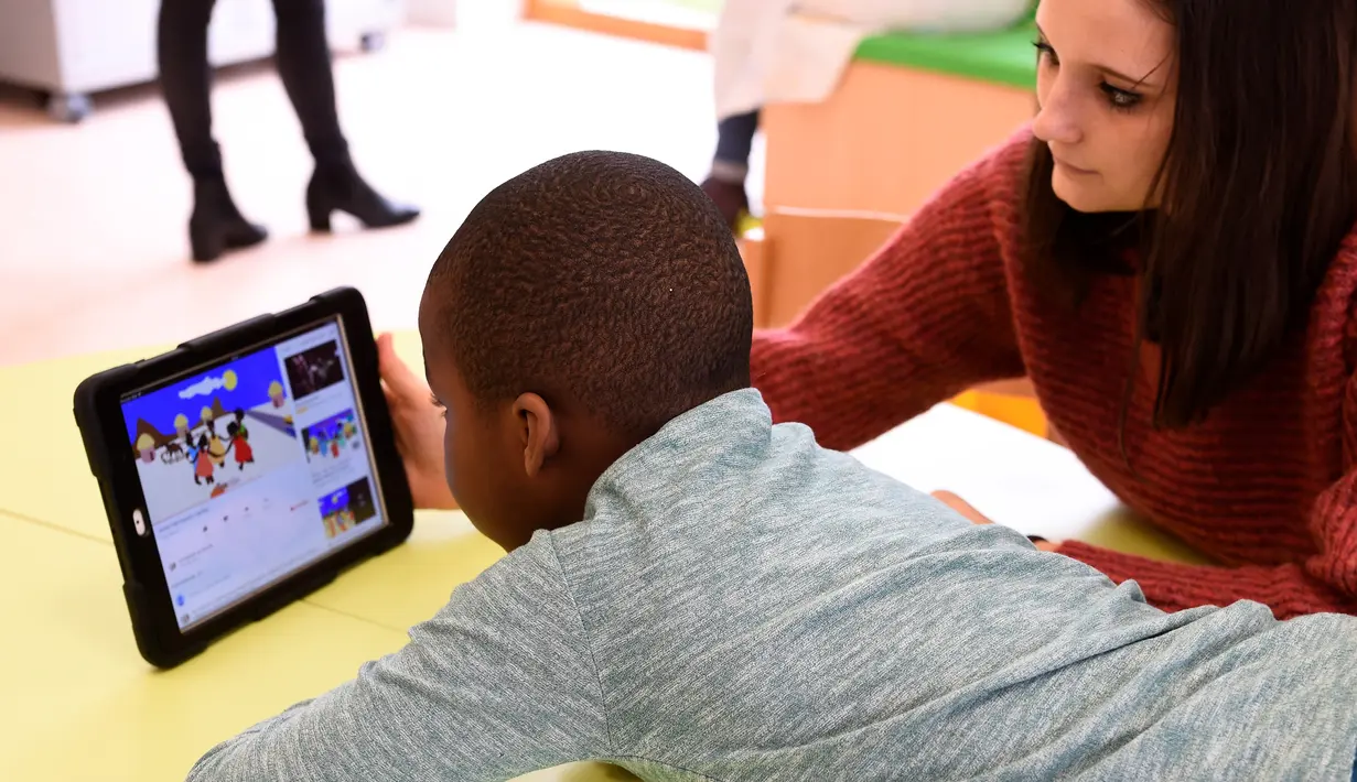 Seorang perawat bersama salah satu anak sedang menonton dari layar tablet di Rumah Sakit Ecole di Neuilly-Plaisance, dekat Paris, 21 Maret 2017. Rumah sakit yang khusus untuk anak penderita autis ini baru saja dibuka untuk umum. (BERTRAND GUAY/AFP)