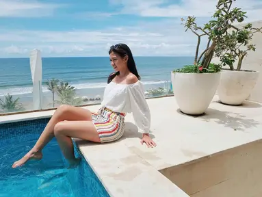 Yuki Kato tampak bahagia saat bermain air di sebuah kolam renang hotel di Bali. Menggunakan pakaian putih dan celana garis-garis warna-warni, latar belakang lautan dan langit biru menambah keindahan pemandangan.(Liputan6.com/IG/@yukikt)