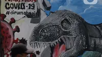 Pengendara motor melintas di depan mural bertema waspada COVID-19 di Jalan Baru, Depok, Jawa Barat, Selasa (7/4/2020). Mural tersebut berisi pesan kepada warga agar selalu waspada potensi penyebaran virus corona atau COVID-19. (Liputan6.com/Helmi Fithriansyah)