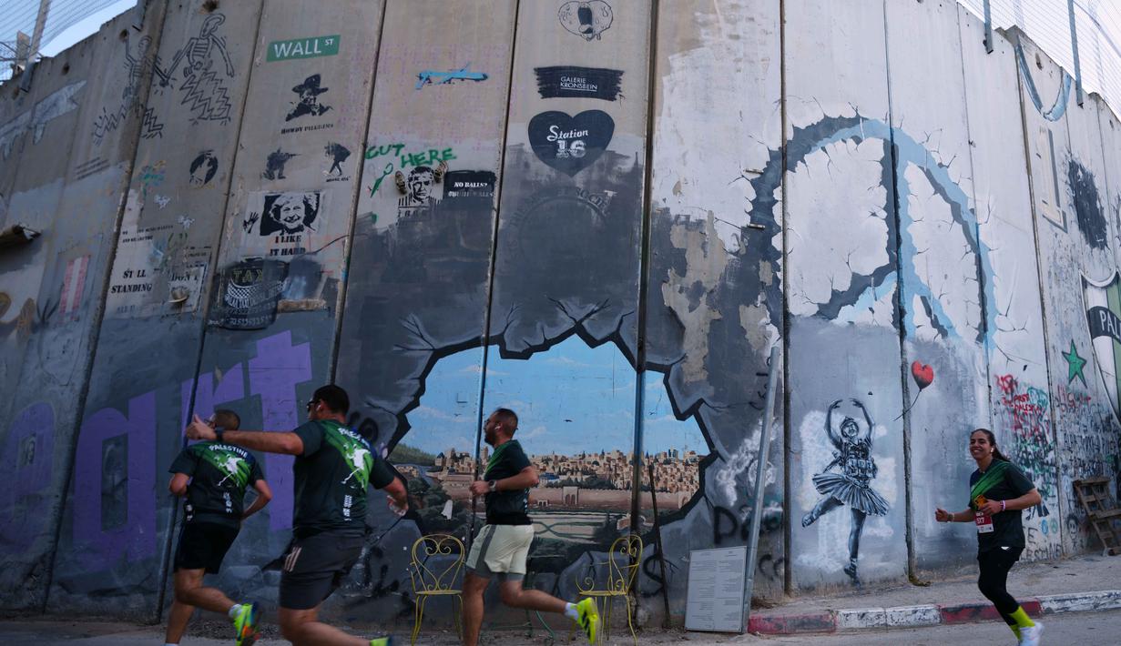 Edisi ke-10 acara ini menandai kembalinya Maraton Internasional Palestina ke jalanan Betlehem setelah sempat terhenti selama dua tahun akibat perang di Gaza. Tampak dalam foto, para pelari melewati tembok pemisah Israel saat mereka berkompetisi dalam Maraton Palestina di kota Betlehem, Tepi Barat, Jumat 8 Mei 2026. (AP Photo/Mahmoud Illean)