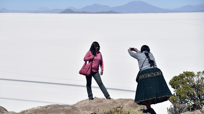 Turis berfoto dengan latar belakang Salar de Uyuni, dataran garam terluas di dunia yang terletak di Altiplano, barat daya Bolivia, 28 September 2019. Hamparan danau yang bisa dipijak itu begitu jernih sehingga membuat pantulan langit di atasnya. (Photo by Aizar RALDES / AFP)