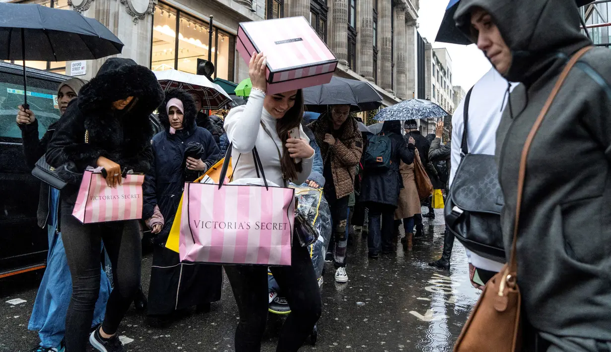 Pemburu diskon berlindung dari hujan dengan belanjaan mereka selama Boxing Day di London, Kamis (26/12/2019). Boxing Day merupakan tradisi hari belanja terbesar tahunan yang diperingati setiap 26 Desember atau sehari setelah Natal dan menjadi hari libur nasional di Inggris. (Niklas HALLE'N/AFP)
