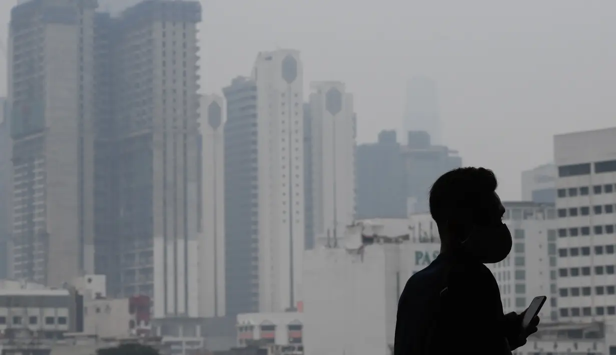 Seorang pria mengenakan masker saat kabut menyelimuti gedung-gedung di Kuala Lumpur (10/9/2019). Malaysia tengah mempersiapkan membuat hujan buatan setelah kualitas udara di sejumlah negara bagian mencapai level yang tidak sehat. (AFP Photo/Mohd Rasfan)