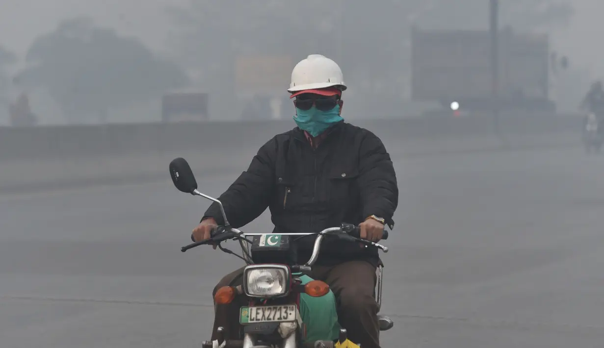 Pengendara motor mengenakan masker saat kabut asap tebal di Lahore (21/11/2019). Akibat kabut asap tebal penduduk Lahore mengeluh sakit tenggorokan, mata gatal dan penyakit lainnya.  (AFP Photo/Arif Ali)