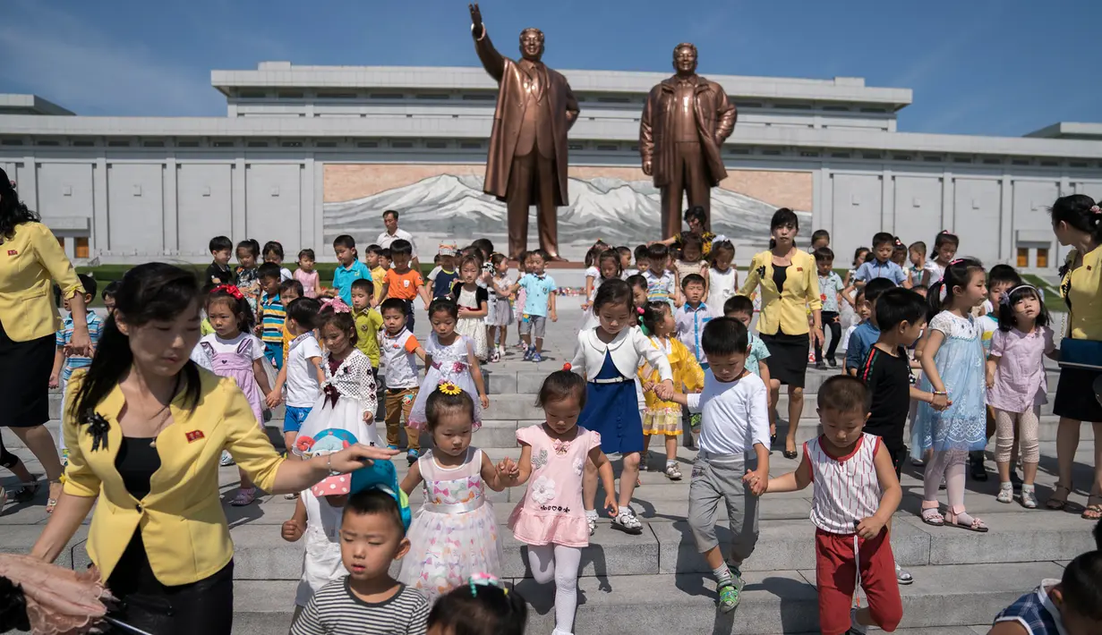 Anak-anak berjalan di depan patung pemimpin Korea Utara Kim Il Sung (kiri) dan Kim Jong Il (kanan), setelah meletakkan bunga untuk menandai peringatan 24 tahun kematian Kim Il Sung, di bukit Mansu, Pyongyang, Minggu (8/7). (AP Photo/Andrew Harnik, Pool)