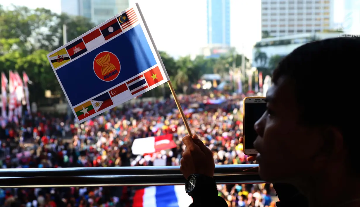 Warga memegang bendera ASEAN saat menonton parade ASEAN 50 Tahun di Jakarta, Minggu (27/8). Acara ini menampilkan Parade Bendera ASEAN, Parade kostum, Parade tari musik, dan keunikan lainnya. (Liputan6.com/Angga Yuniar)