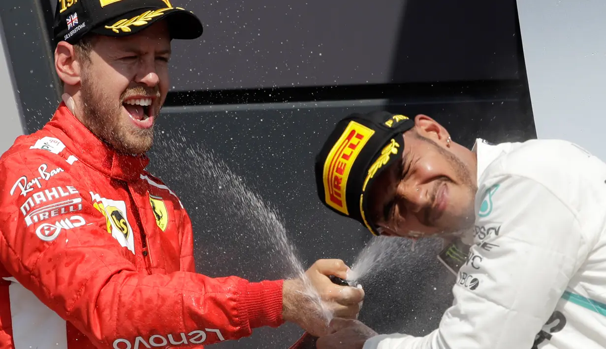 Pembalap Ferrari, Sebastian Vettel (kiri) menyemprotkan sampanye kepada pembalap Mercedes Lewis Hamilton usai memenangkan F1 GP di Sirkuit Silverstone, Inggris, Minggu (8/7). Vettel berhasil mengungguli Lewis Hamilton. (AP Photo/Luca Bruno)