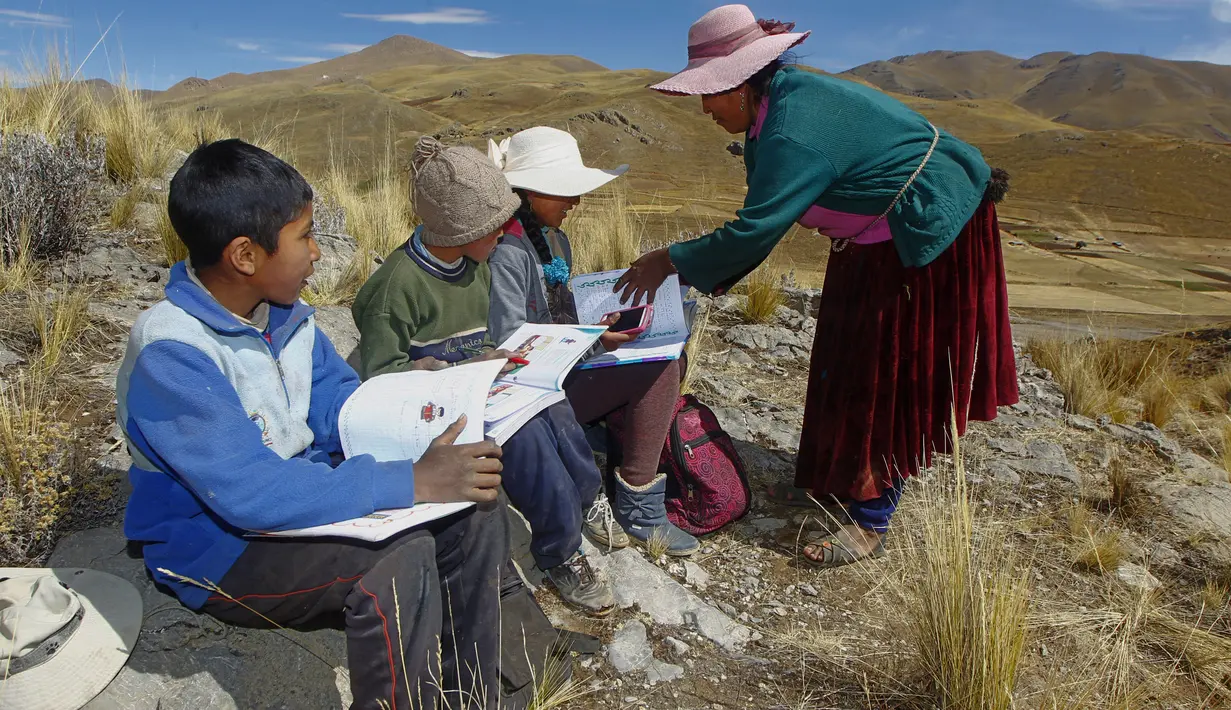 Raymunda Charca membantu anak-anaknya saat menghadiri kelas virtual selama pandemi COVID-19 di atas bukit di komunitas dataran tinggi Conaviri yang terpencil di Andes Peru, 24 Juli 2020. Mereka harus naik ke puncak bukit untuk mencari sinyal ponsel untuk menghadiri kelas virtual. (Carlos MAMANI/AFP)