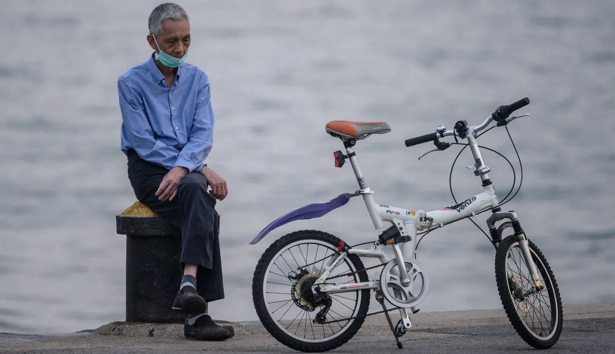 Seorang pria mengenakan masker beristirahat di samping sepedanya di tambatan di kargo yang dijuluki 'Instagram Pier' di Hong Kong (21/4/2020). Hong Kong melaporkan penurunan kasus infeksi harian Covid-19, tetapi pemerintah kota mengatakan mereka tidak mengambil risiko apa pun. (AFP/Anthony Wallace)