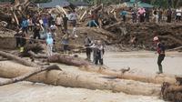 Warga yang menjadi korban banjir bandang di Batang Toru, Tapanuli Selatan, Sumatra Utara menggunakan kayu gelondongan untuk menyeberangi sungai, Selasa 2 Desember 2025. Warga Batang Toru, Tapanuli Selatan, terpaksa menggunakan jembatan darurat yang terbuat dari gelondongan kayu untuk menyeberangi sungai setelah jembatan utama rusak akibat terjangan banjir bandang baru-baru ini. (AP Photo/Binsar Bakkara)