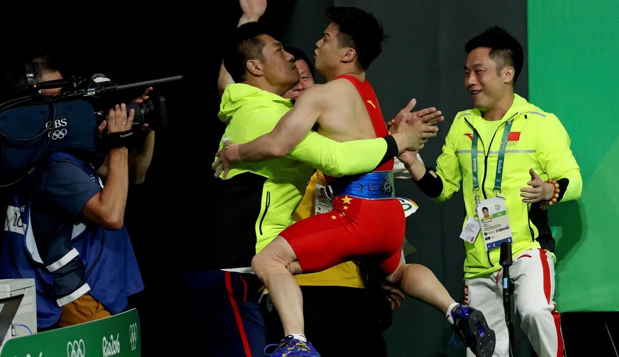 Atlet angkat besi putra China, Long Qingquan melakukan selebrasi dengan memeluk pelatihnya usai meraih kemenangan pada angkat besi 56kg putra di Olimpiade Rio 2016, Brasil (7/8). Long Qingquan meraih emas pada Olimpiade 2016. (REUTERS/Stoyan Nenov)