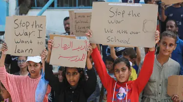 Sejumlah pelajar didampingi para aktivis Palestina mengangkat plakat saat berunjuk rasa menyerukan diakhirinya situasi perang di Gaza, di samping gedung sekolah yang rusak di Khan Yunis di Jalur Gaza selatan pada 28 Agustus 2024. (Bashar TALEB/AFP)