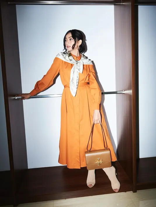Tampil retro dengan gaun panjang berwarna oranye serta aksesoris dan tas kulit coklat, membuat hasil foto penyanyi, aktris dan model ini ala klasik 90-an. (Liputan6.com/IG/@glencachysaraofficial)
