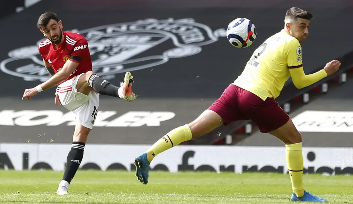Pemain Manchester United Bruno Fernandes menendang bola di depan pemain Burnley Matthew Lowton pada pertandingan Liga Inggris di Stadion Old Trafford, Manchester, Inggris, Minggu (18/4/2021). Manchester United menang 3-1. (Martin Rickett/Pool via AP)