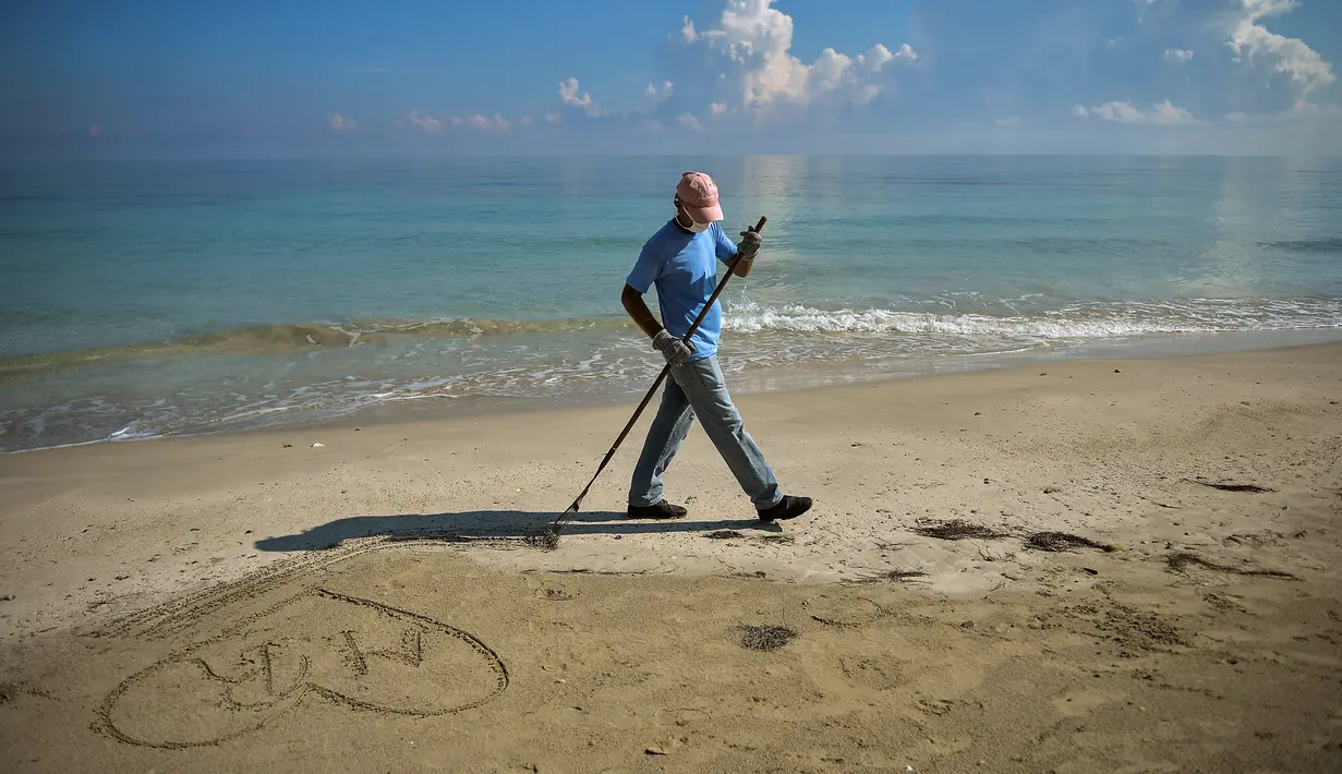 Seorang pekerja dengan mengenakan masker membersihkan pantai di Havana pada Senin (15/6/2020). Kuba akan menguji semua pelancong untuk Covid-19 dan membatasi kontak mereka dengan penduduk setempat ketika perbatasan dibuka kembali untuk turis asing. (Yamil LAGE / AFP)