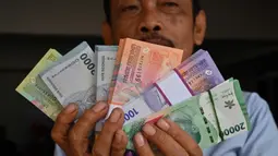 Seorang pria menunjukkan uang kertas Rupiah yang baru, yang akan diberikan kepada anggota keluarganya saat perayaan Idul Fitri, di Jakarta pada 28 Maret 2024. (Adek BERRY/AFP)