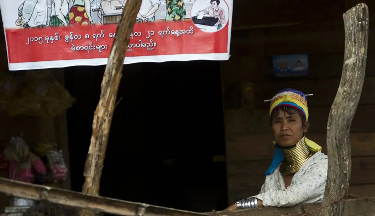 Wanita etnis Kayan duduk di sebelah poster pemilu di desa PanPat, Kayan, Myanmar, Rabu (9/9/2015). Kaum perempuan Suku Kayan ini mengenakan banyak kalung berbentuk cincin di lehernya hingga membuat leher mereka panjang. (AFP PHOTO/Ye Aung THU)