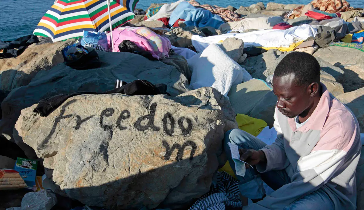 Seorang imigran membaca Al-Quran saat bulan suci ramadan di atas bebatuan laut Ventimiglia, perbatasan antara Italia-Prancis, (18/6/2015). Sekitar 200 imigran berada di bebatuan pantai untuk melintasi perbatasan Italia. (REUTERS/Eric Gaillard)