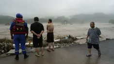 Seorang pekerja penyelamat dan warga lainnya melihat ke arah sungai yang meluap di daerah Miaofengshan di pinggiran Beijing, Selasa, 1 Agustus 2023. (AP Photo/Ng Han Guan)