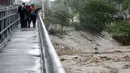 Warga menyeberangi jembatan dimana air telah naik akibat hujan yang disebabkan oleh Badai Matthew melewati Port-au-Prince, Haiti, (4/10). (REUTERS/Carlos Garcia Rawlins)