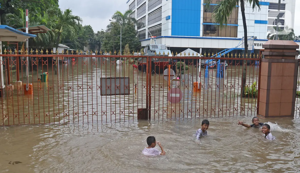 Anak-anak bermain air saat banjir merendam halaman pintu masuk Kantor Direktorat Jenderal Bea dan Cukai di Jakarta, Selasa (25/2/2020). Hujan yang mengguyur Jakarta sejak dini hari tadi membuat halaman Kantor Direktorat Jenderal Bea dan Cukai terendam banjir. (Liputan6.com/Herman Zakharia)