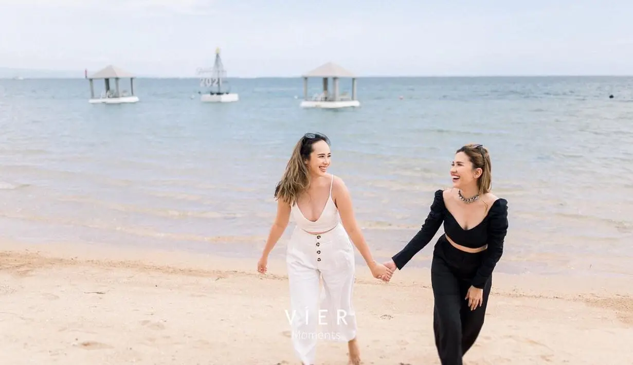Tampil menggemaskan, Pamela Bowie berpose bergandengan tangan dengan sahabatnya mengenakan crop top tanpa lengan bertali spageti. Ia padukan dengan celana panjang dengan detail kancing di bagian tengah atas, yang bernuansa putih yang senada. Foto: Instagram.