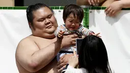 Seorang pesumo menggendong bayi sebelum dimulainya kejuaraan sumo, Honozumo, di Kuil Yasukuni, Tokyo, Senin (18/4). Selain menjadi ajang kejuaraan olahraga tradisional jepang, kejuaraan tahunan itu juga menjadi daya tarik wisata. (REUTERS/Yuya Shino)