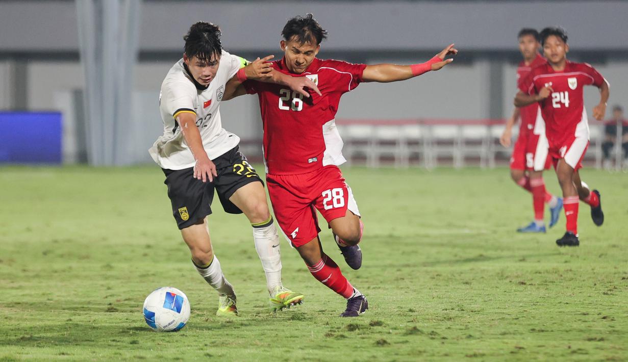 Pemain Timnas Indonesia U-17, I Komang Semadi berduel dengan pemain China U-17, Li Junpeng dalam pertandingan uji coba internasional di Indomilk Arena, Tangerang, pada Rabu (11/2/2026) malam WIB. (Bola.com/Abdul Aziz)