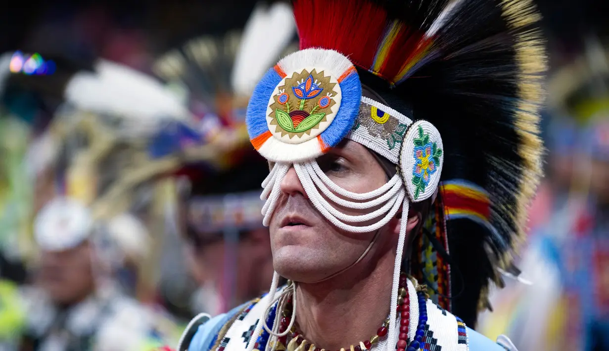 Seorang pria mengenakan kostum dan atribut kepala bersiap mengikuti Grand Entry of the Denver March Powwow di Denver, Colorado (24/3). (AFP/Jason Connolly)