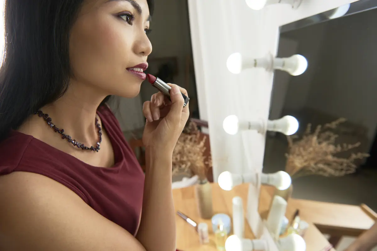 Seorang perempuan sedang bercermin sembari mengenakan lipstik (Foto Dok: Freepik/pressfoto)