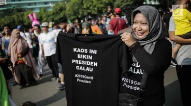 Pedagang memperlihatkan kaus #2019GantiPresiden yang dijajakan saat Car Free Day di kawasan Bundaran HI, Jakarta, Minggu (29/4). Memanasnya suasana politik nasional dimanfaatkan pedagang berjualan atribut #2019GantiPresiden. (Liputan6.com/Faizal Fanani)
