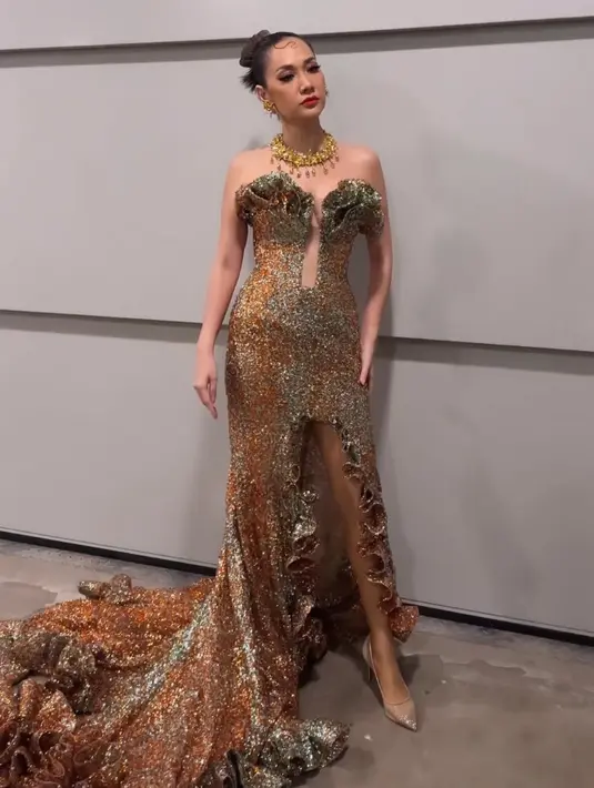 Bunga Citra Lestari tampil dibalut tube dress model slit warna keemasan dari Yogie Pratama. Dipadukan kalung dan anting emas dari Tulola. [@andreblanke_]