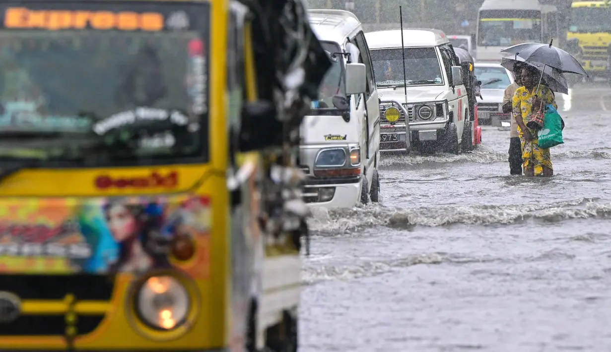 Sejumlah aktivitas warga di luar ruangan dihentikan sementara, termasuk sekolah dan layanan kereta api. Tampak dalam foto, orang-orang berjalan di jalan yang terendam banjir di Biyagama, pinggiran Kolombo, pada Jumat 28 November 2025. (Ishara S. KODIKARA/AFP)