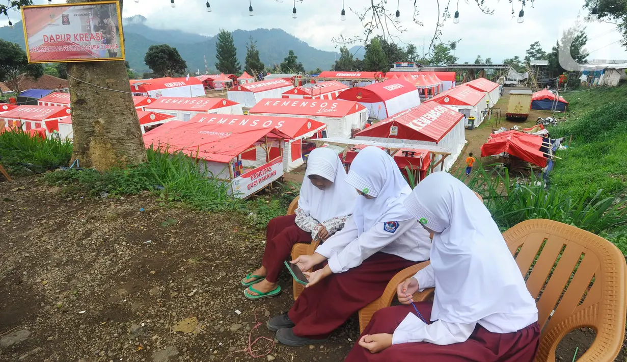 Warga bermain hp di kawasan  hunian sementara penyintas  gempa di Desa Mangunkerta, Cianjur, Jumat (23/12/2022). Lebih dari sebulan sejak musibah gempa bumi 5,2 SR sejumlah warga masih tinggal di pengungsian dan hunian sementara dengan bantuan kebutuhan hidup dari para donatur. (merdeka.com/Arie Basuki)