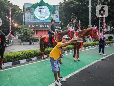 Warga berswafoto dengan polisi berkuda yang bersiaga saat hari bebas kendaraan bermotor (HBKB) atau car free day (CFD) di kawasan Bundaran HI, Jakarta, Minggu (23/7/2023). Selain bagian dari pengamanan, kehadiran polisi berkuda ini juga menjadi sarana wisata yang menghibur warga saat beraktivitas di CFD. (Liputan6.com/Faizal Fanani)