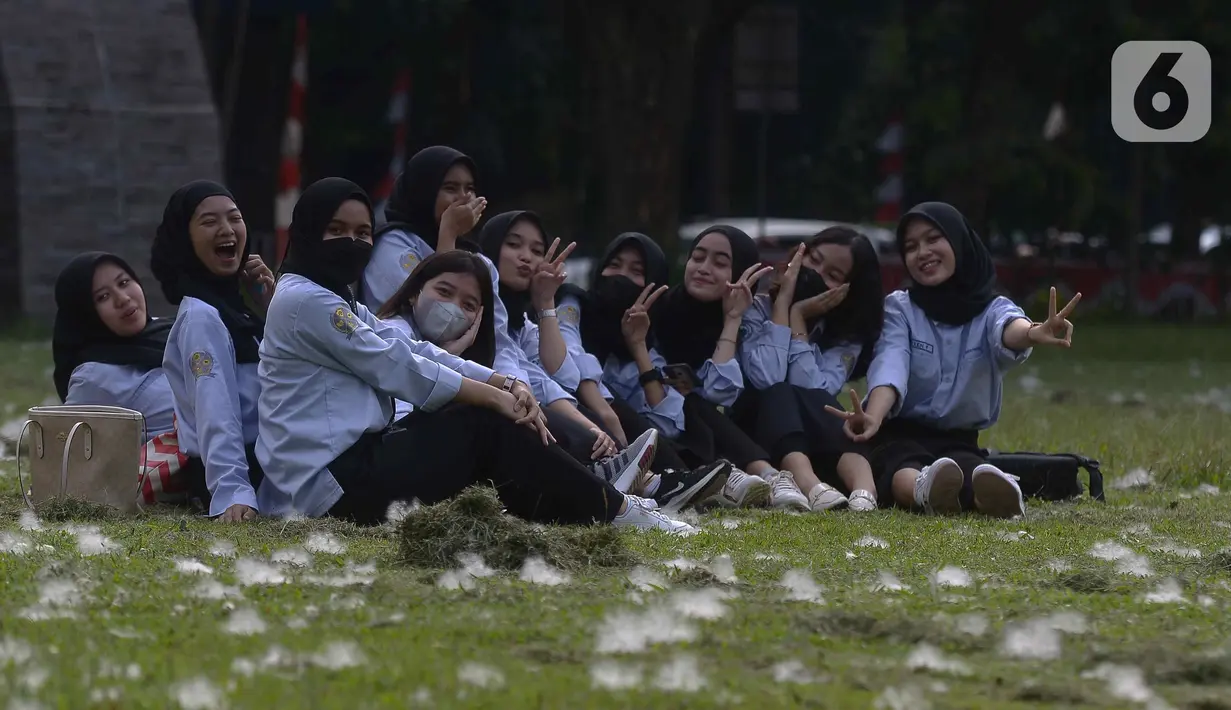Mahasiswa berfoto di rumput yang bercampur dengan kapas di halaman Institut Pertanian Bogor, Kota Bogor, Jawa Barat, Kamis (25/8/2022). Kapas yang berasal dari pohon kapuk randu yang sedang berguguran itu menjadi daya tarik bagi warga untuk berswafoto. (Liputan6.com/Angga Yuniar)