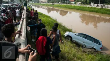 Warga menyaksikan proses evakuasi mobil yang terperosok di saluran Ispeksi Kalimalang, Jabar, Minggu (7/5). Minibus bernopol B 1475 FRK itu tercebur kedalam saluran inspeksi Kalimalang dan sempat terseret arus sejauh 100m. (Liputan6.com/Gempur M Surya)