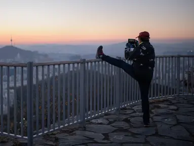 Seorang pejalan kaki mengabadikan kota Seoul dan menara Namsan dengan ponselnya selama matahari terbit di Korea Selatan (31/10). Seoul adalah ibu kota Korea Selatan yang berusia lebih dari 600 tahun. (AFP Photo/Ed Jones)